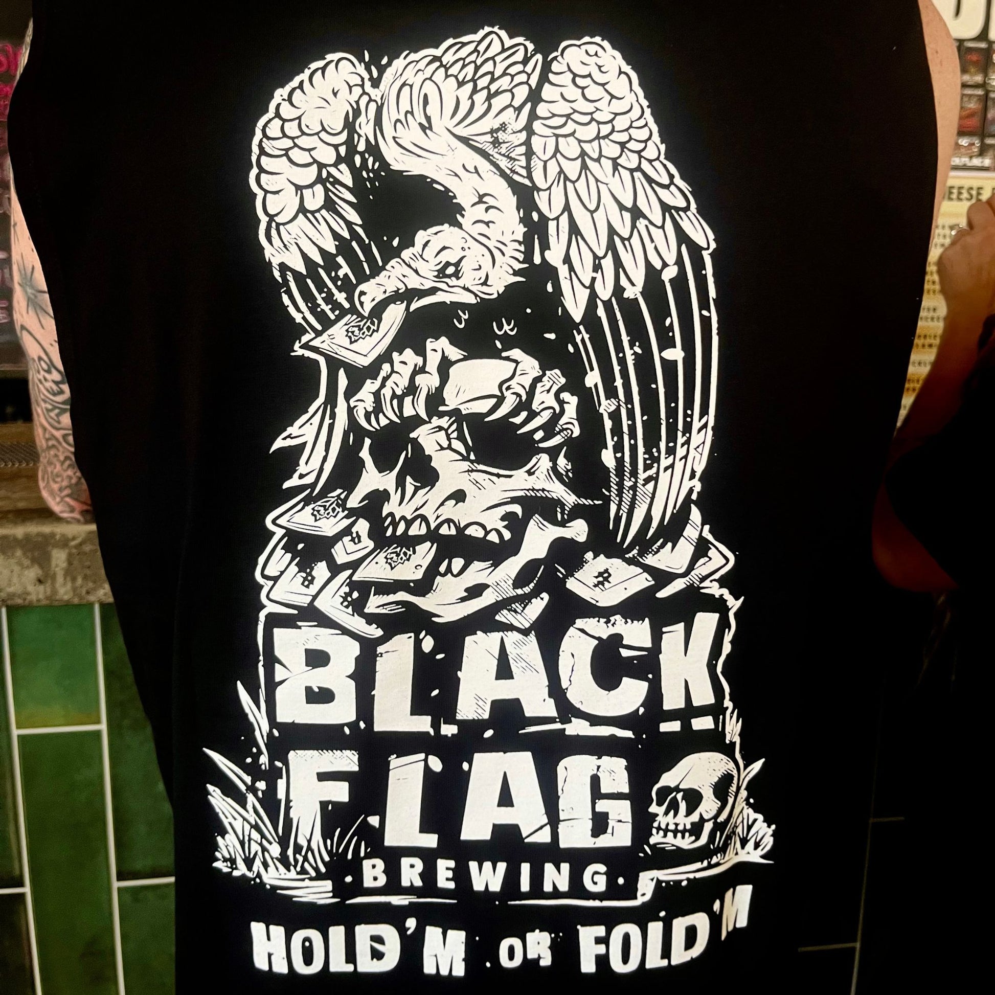 Man wearing a black Blackflag tank top with hand drawn Hold ‘Em Or Fold ‘Em illustration on back.