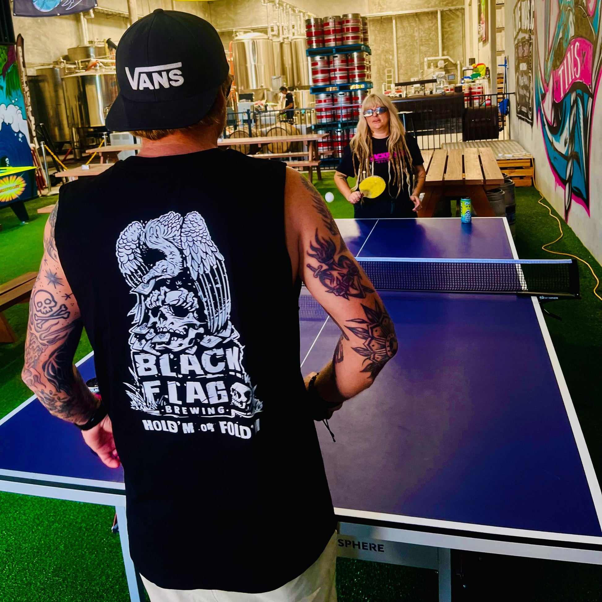 Man wearing a black Blackflag tank top with hand drawn Hold ‘Em Or Fold ‘Em illustration on back.